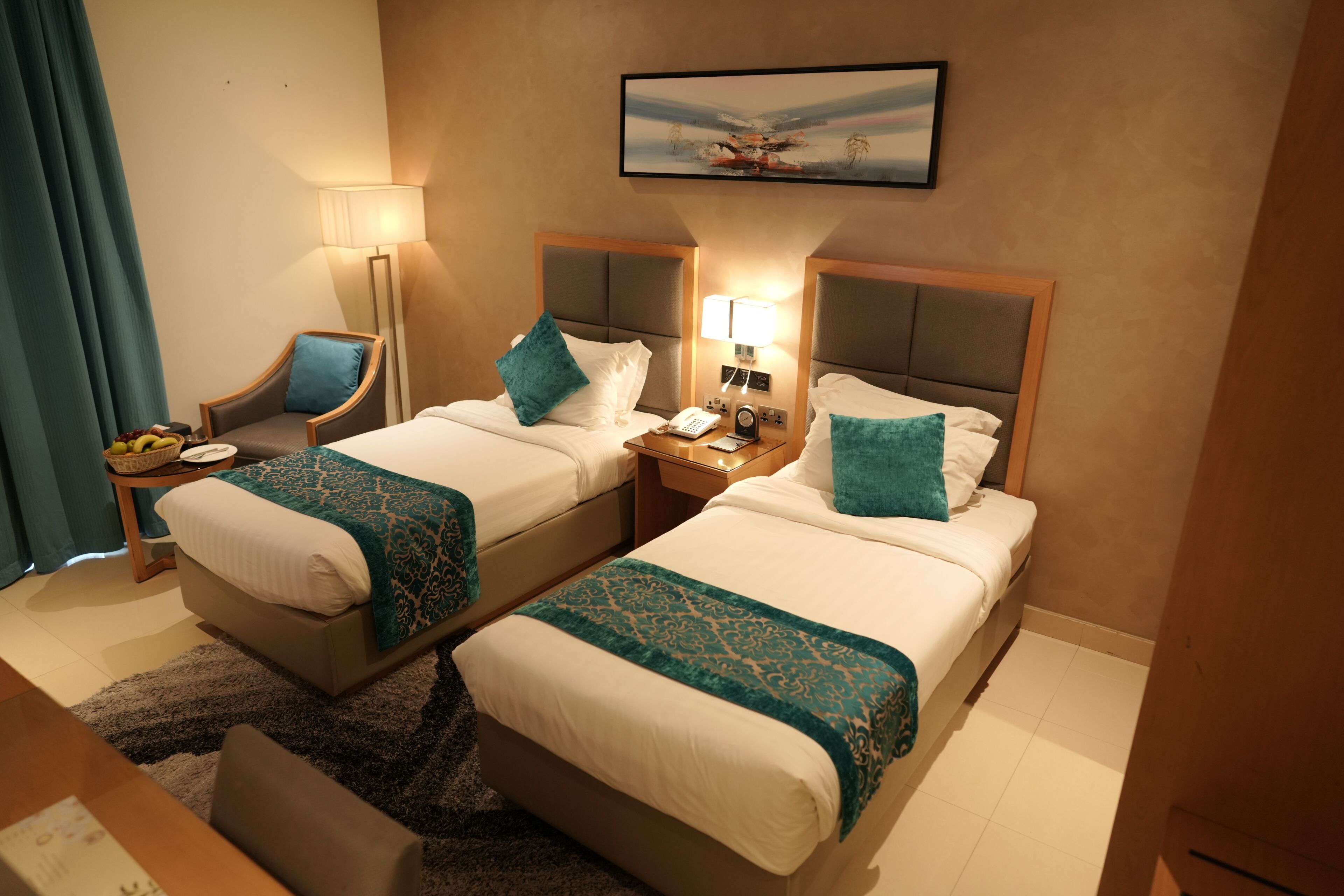 A hotel room with two beds, a desk, a chair, a lamp, a nightstand, and a painting on the wall.