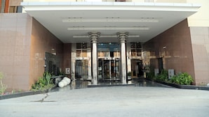 Una entrada moderna a un edificio con un vestíbulo cubierto, columnas grandes y una puerta de cristal.