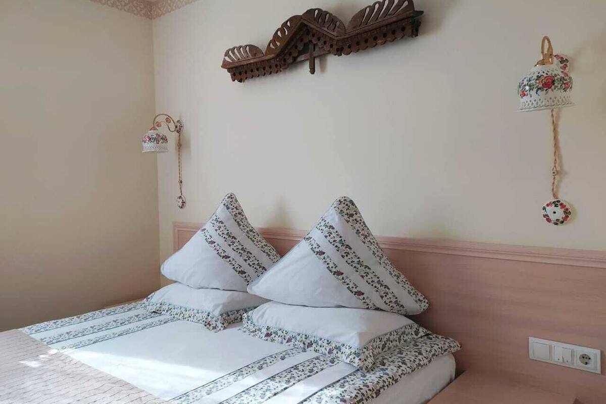 A neatly made bed with patterned bedding, a wooden headboard, and decorative wall hangings.
