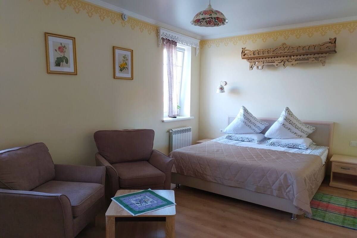 A bedroom with a bed, two chairs, a small table, and a window with curtains.