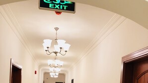 Een hotelgangen met een kroonluchter, een vluchtroutebord en een houten deur aan de rechterkant.