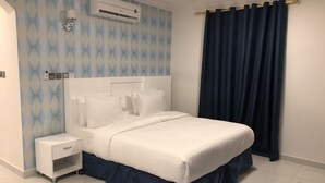 Een moderne slaapkamer met een groot bed, een nachtkastje, een wandairconditioner en een donker gordijn.