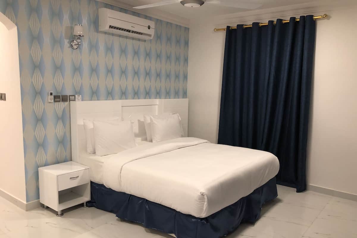 Ein modernes Schlafzimmer mit einem großen Bett, einem Nachttisch, einer Wand-Klimaanlage und einem dunklen Vorhang.
