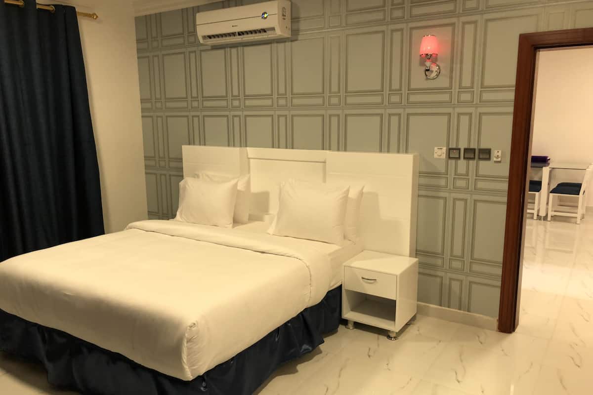 Ein Hotelzimmer mit einem großen Bett, einem Nachttisch, einer Wandklimaanlage und einem kleinen Tisch mit Stühlen in der Ecke.