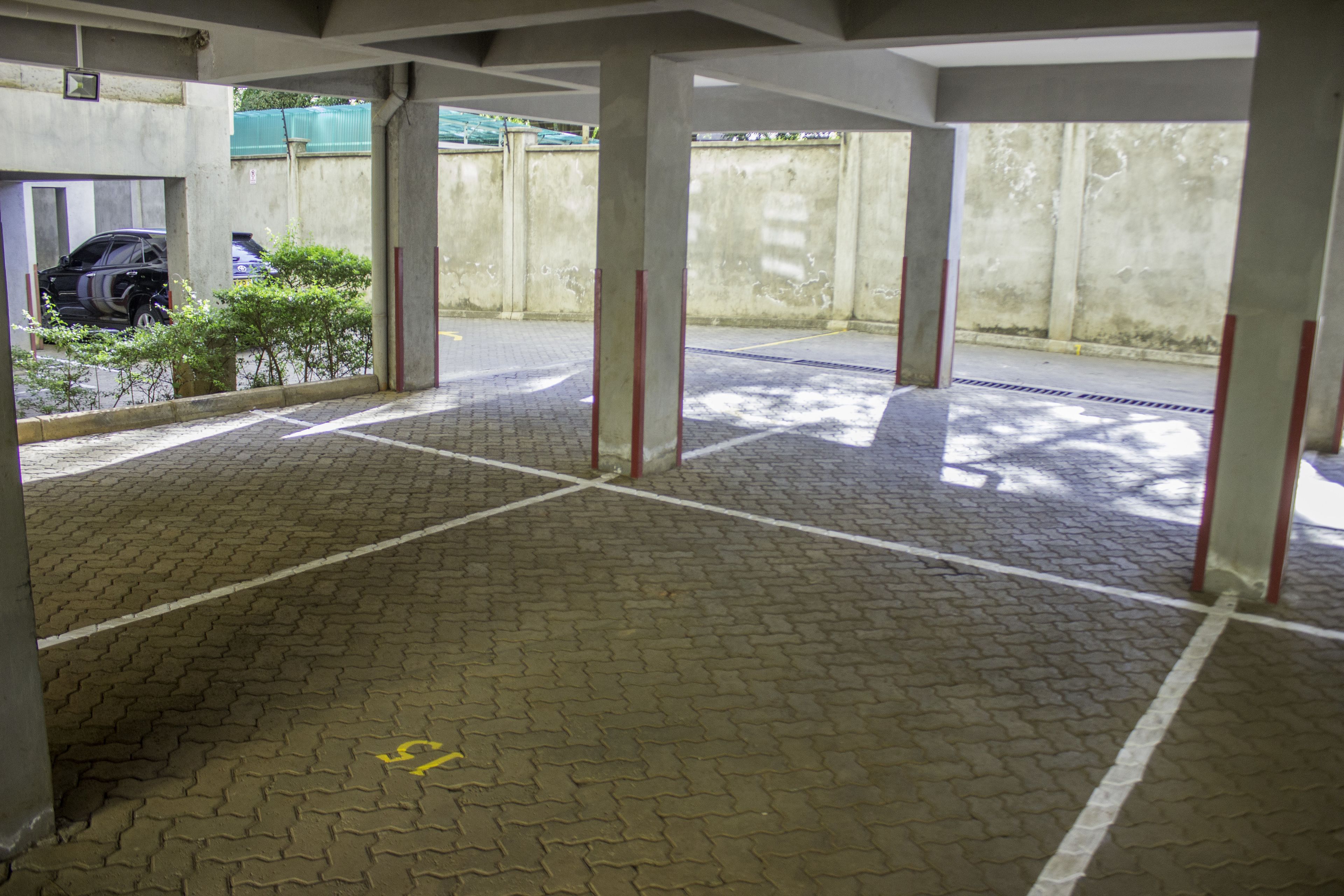Un área de estacionamiento techada con suelo de baldosas y pilares de hormigón.