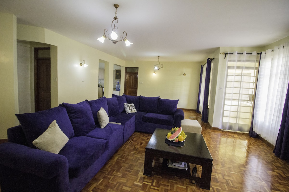 A living room with a sectional sofa, a coffee table with fruit, wooden flooring, and a chandelier.