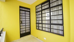 Quarto com paredes amarelas, piso ladrilhado e duas janelas com molduras pretas e vidro fosco.