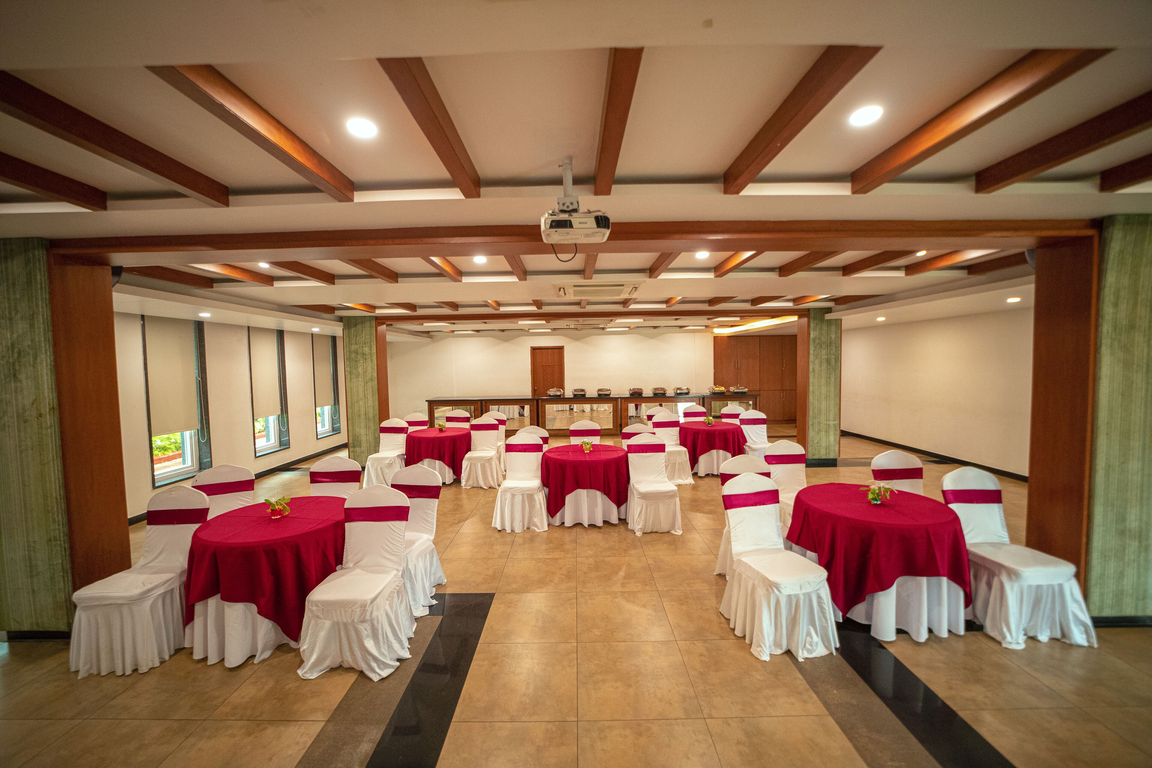 A banquet hall with round tables covered in red tablecloths and white chairs, arranged in rows.