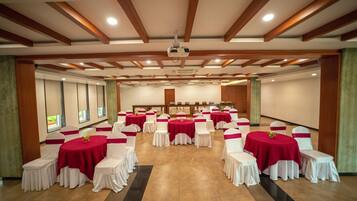 A banquet hall with round tables covered in red tablecloths and white chairs, arranged in rows.