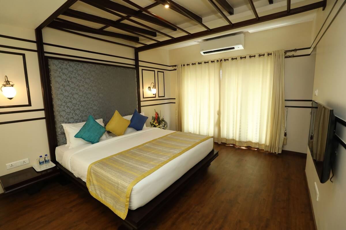 A hotel room with a large bed, wooden floor, a flat-screen TV, and a ceiling fan.