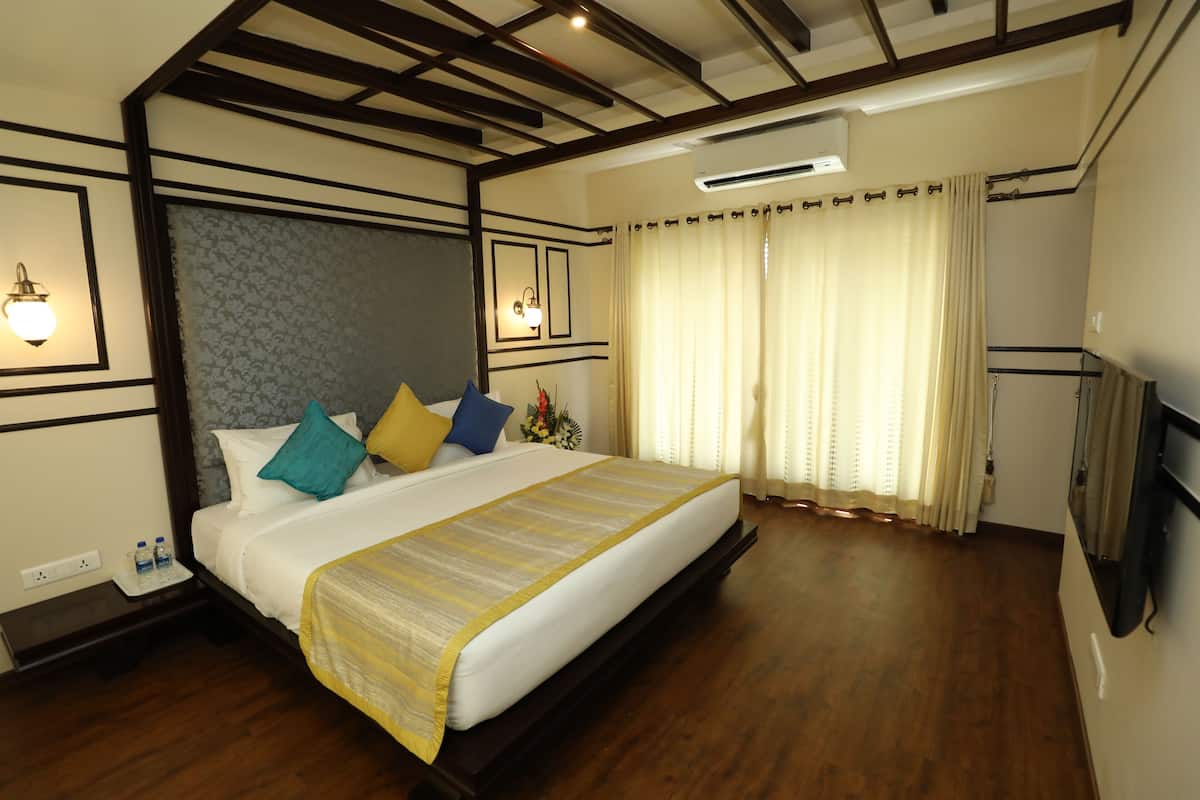 A hotel room with a large bed, wooden floor, a flat-screen TV mounted on the wall, and a ceiling fan.