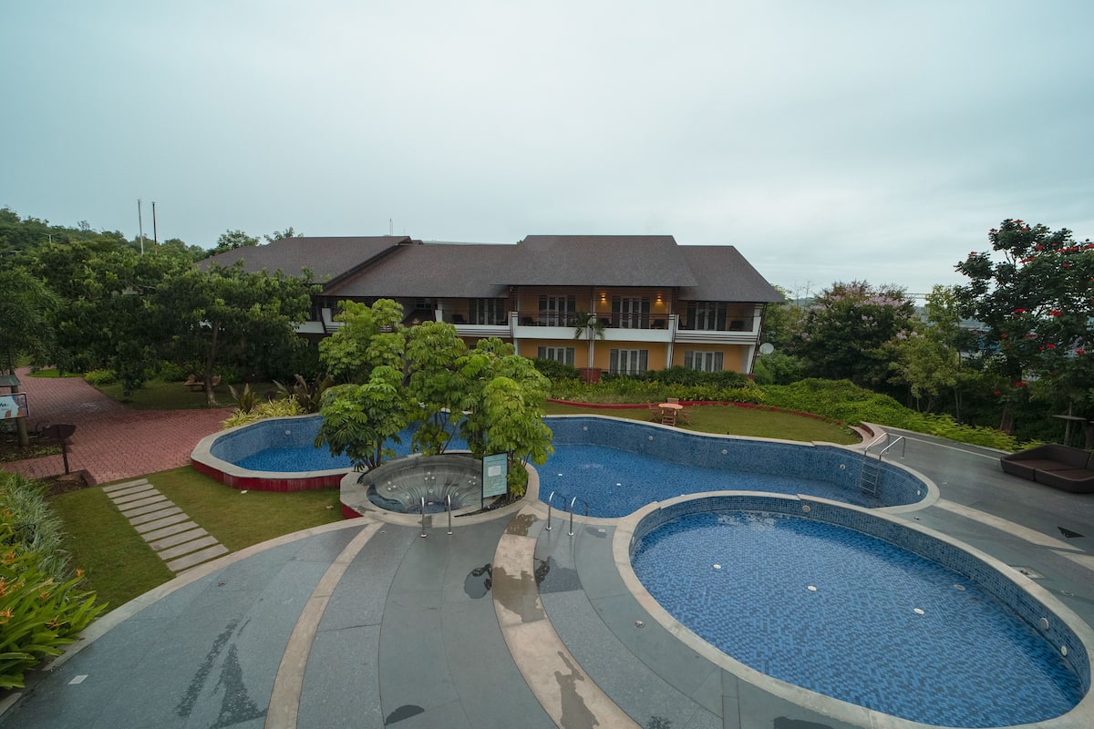 A hotel with a large outdoor swimming pool area, a covered patio, and lush greenery.