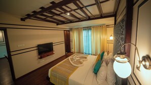 A hotel room with a wooden ceiling, a flat-screen TV mounted on the wall, a bed with a striped bedspread, and a bedside lamp. - The Ocean Pearl Resort And Spa (Dharwad)
