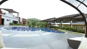 A swimming pool with a curved design, surrounded by outdoor seating areas and a building with balconies. - The Ocean Pearl Resort And Spa (Dharwad)