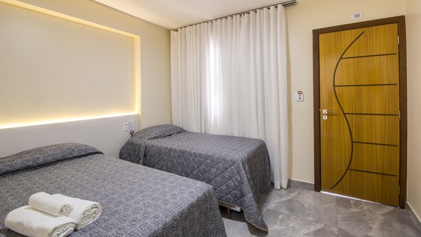 Habitación de hotel con dos camas, una puerta de madera y una cortina.