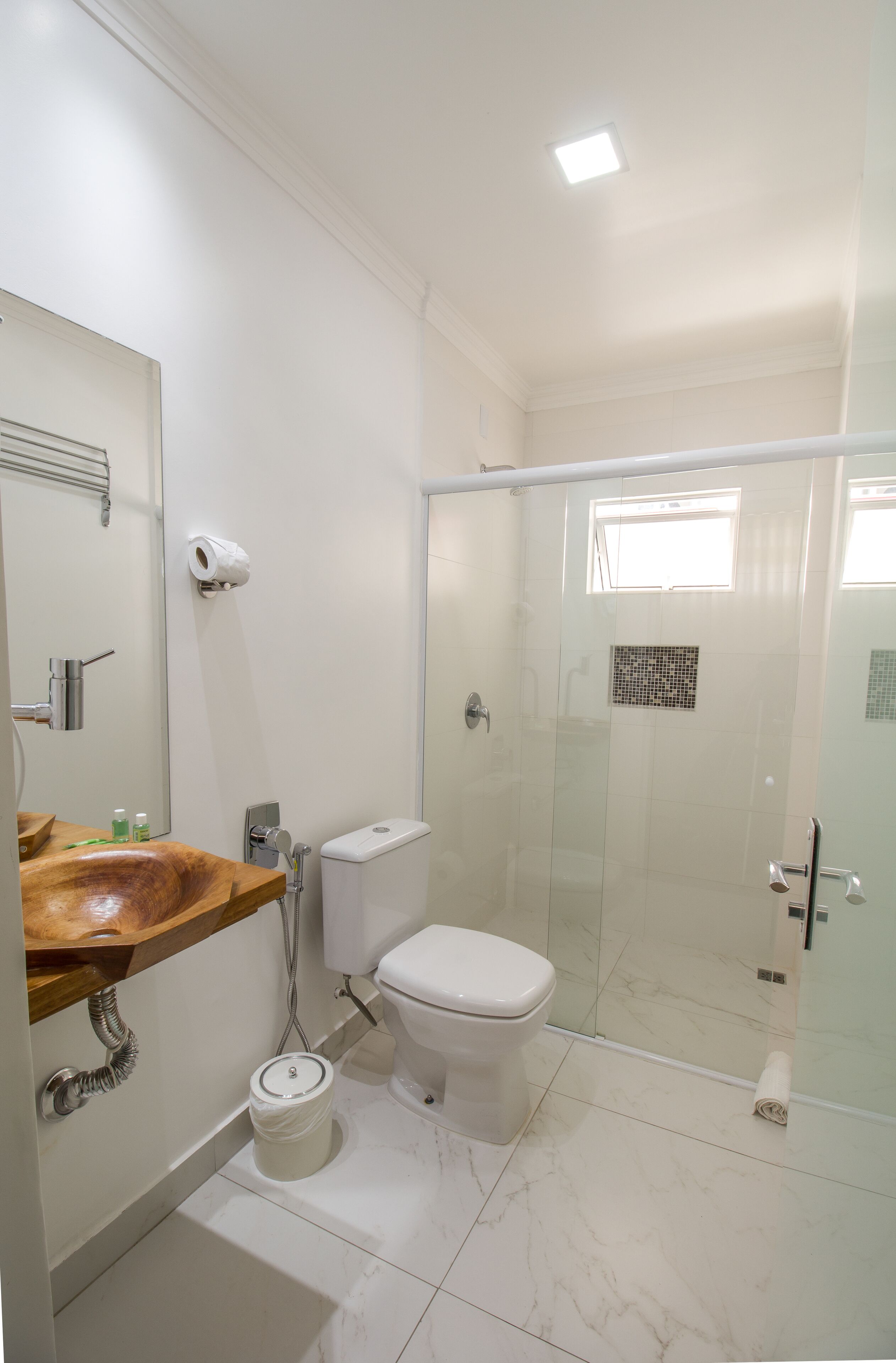 Un baño con tocador de madera, inodoro, cabina de ducha de vidrio y una ventana pequeña.