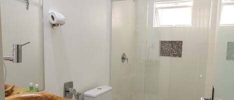 Un baño con tocador de madera, inodoro, cabina de ducha de vidrio y una ventana pequeña.