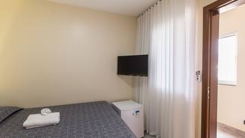Quarto de hotel com cama, pequeno frigorífico branco, televisão de ecrã plano na parede e porta com janela.