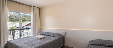 A bedroom with a bed, a bedside table, a window with curtains, and a view of the outside.