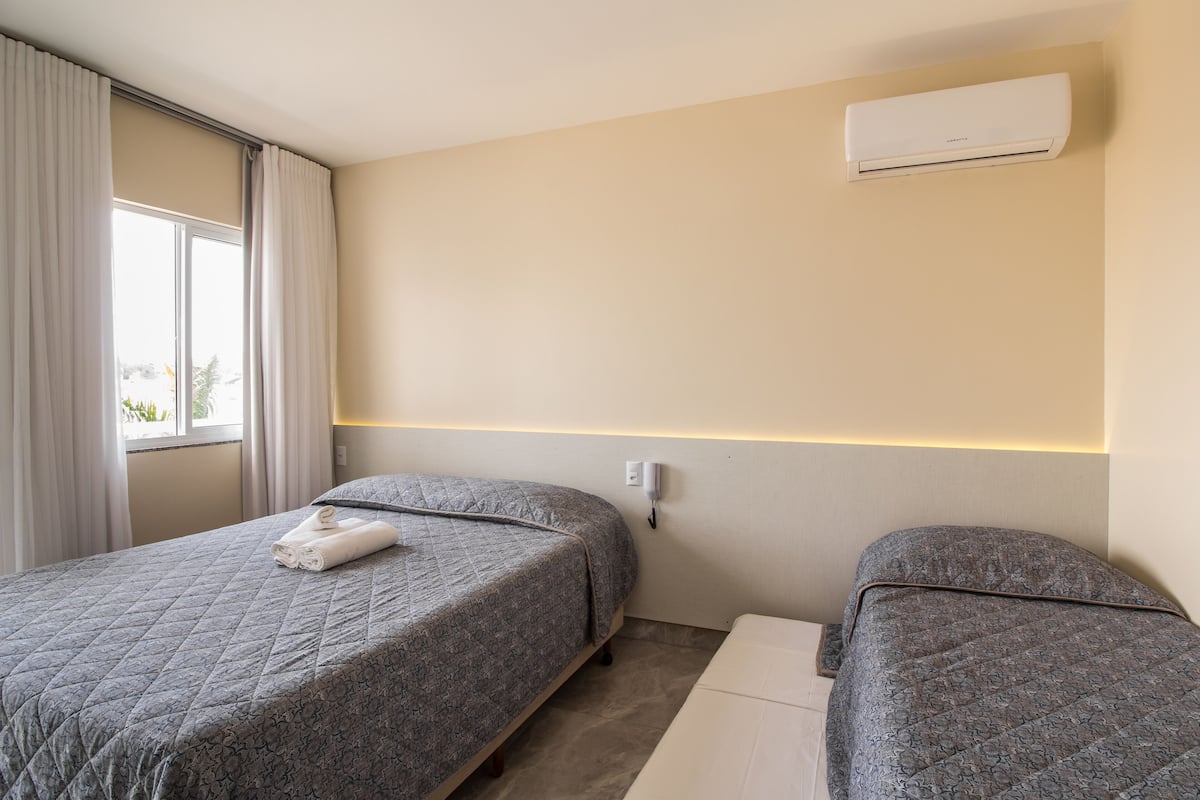 Habitación de hotel con dos camas, una ventana con cortinas, un equipo de aire acondicionado y una mesita de noche.