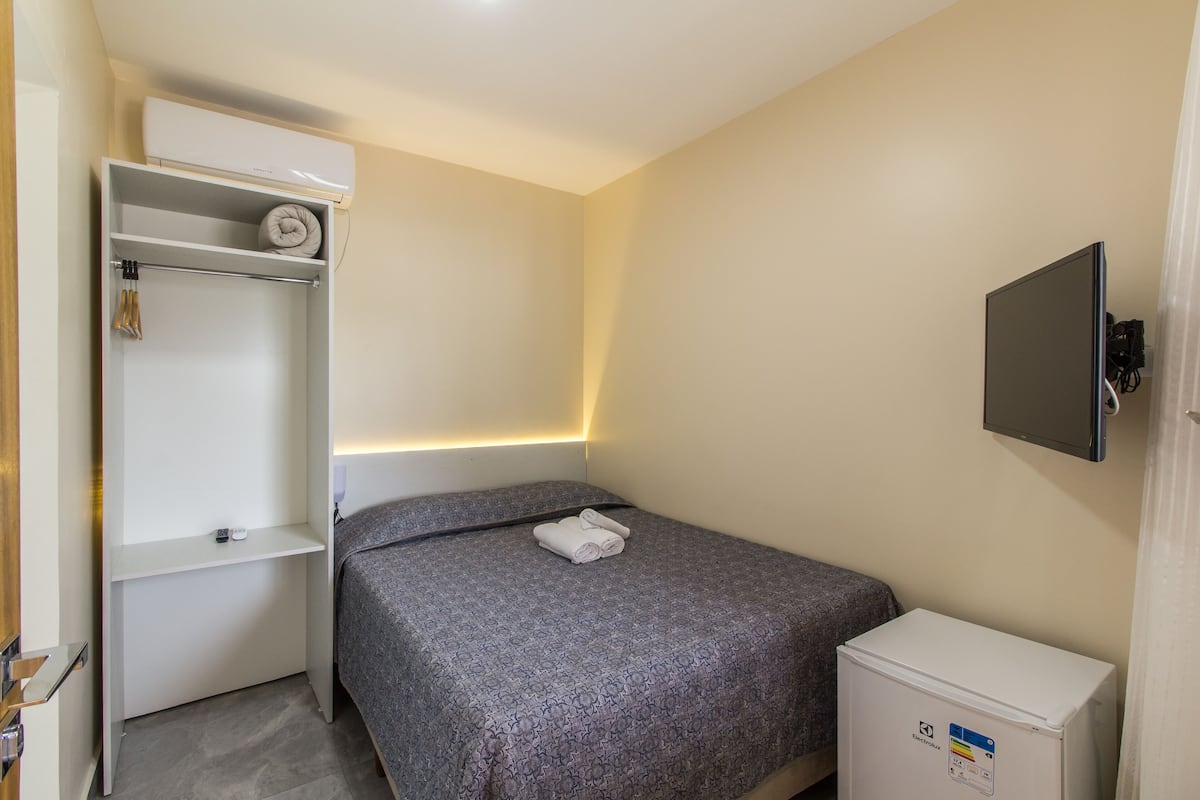 Una habitación de hotel pequeña y ordenada, con una cama, un armario, un mueble bajo y un televisor montado en la pared.