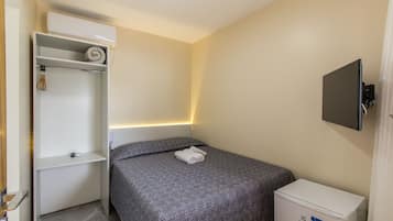 Una habitación de hotel pequeña y ordenada, con una cama, un armario, un mueble bajo y un televisor montado en la pared.
