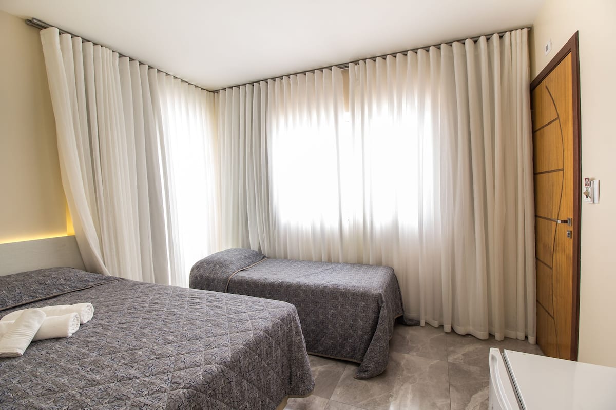 Una habitación de hotel con dos camas, una puerta de madera y un amplio ventanal con cortinas.