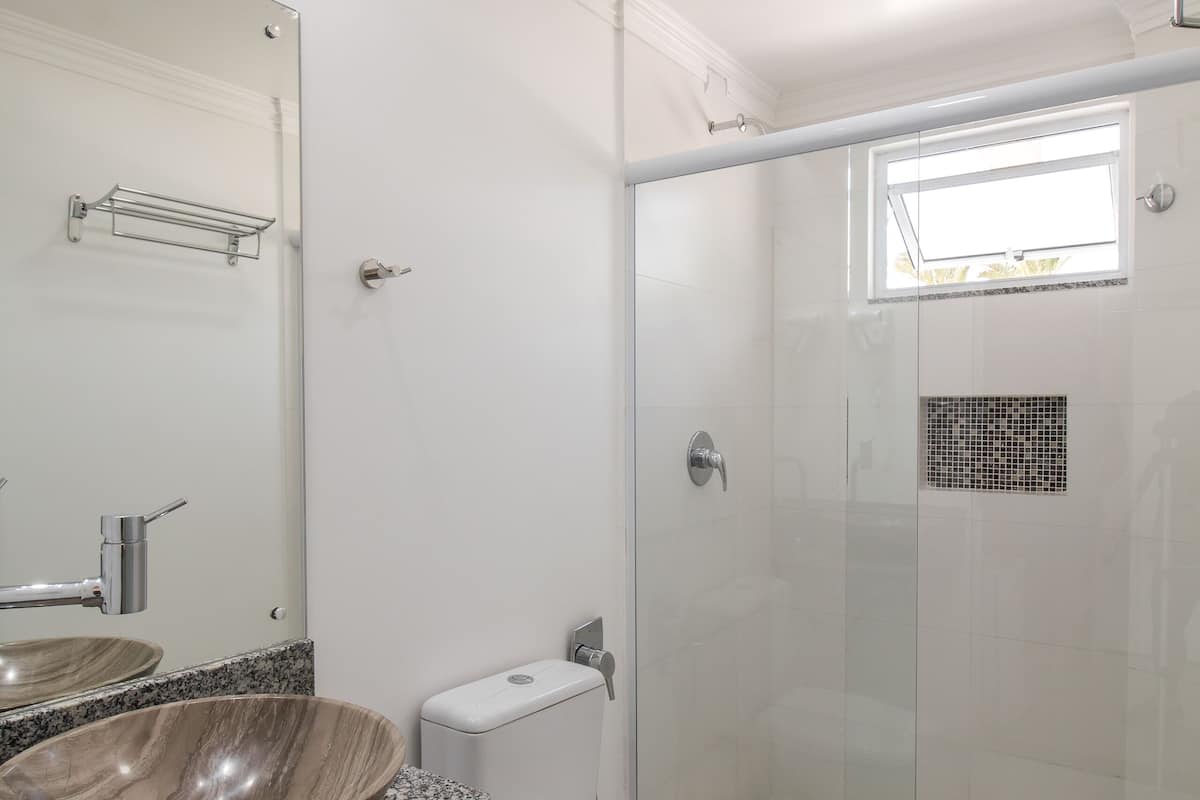 Un baño moderno con un espejo grande, encimera de granito, lavabo sobre encimera, inodoro y ducha con mampara de vidrio.