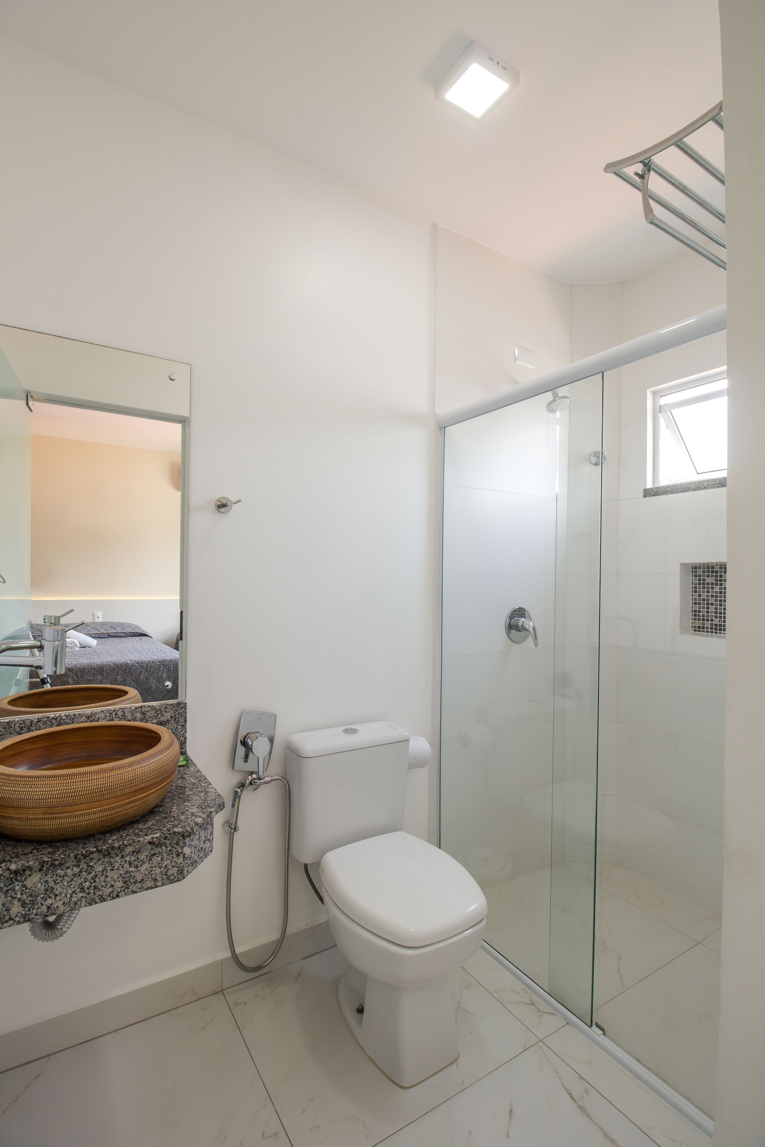 Een moderne badkamer met een douchecabine van glas, een wit toilet en een granieten aanrechtblad met een wastafel van hout.