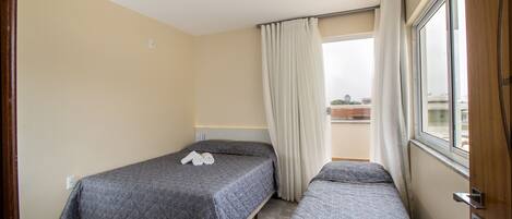 Een kleine hotelkamer met enkel bedden, een raam met gordijnen en een uitzicht op de stad.