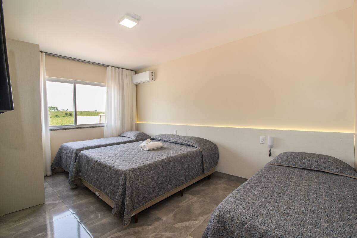 Habitación de hotel con dos camas, un ventanal con cortinas, un equipo de aire acondicionado y una televisión de pantalla plana.