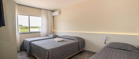A hotel room with two beds, a large window with curtains, an air conditioning unit, and a flat-screen TV.