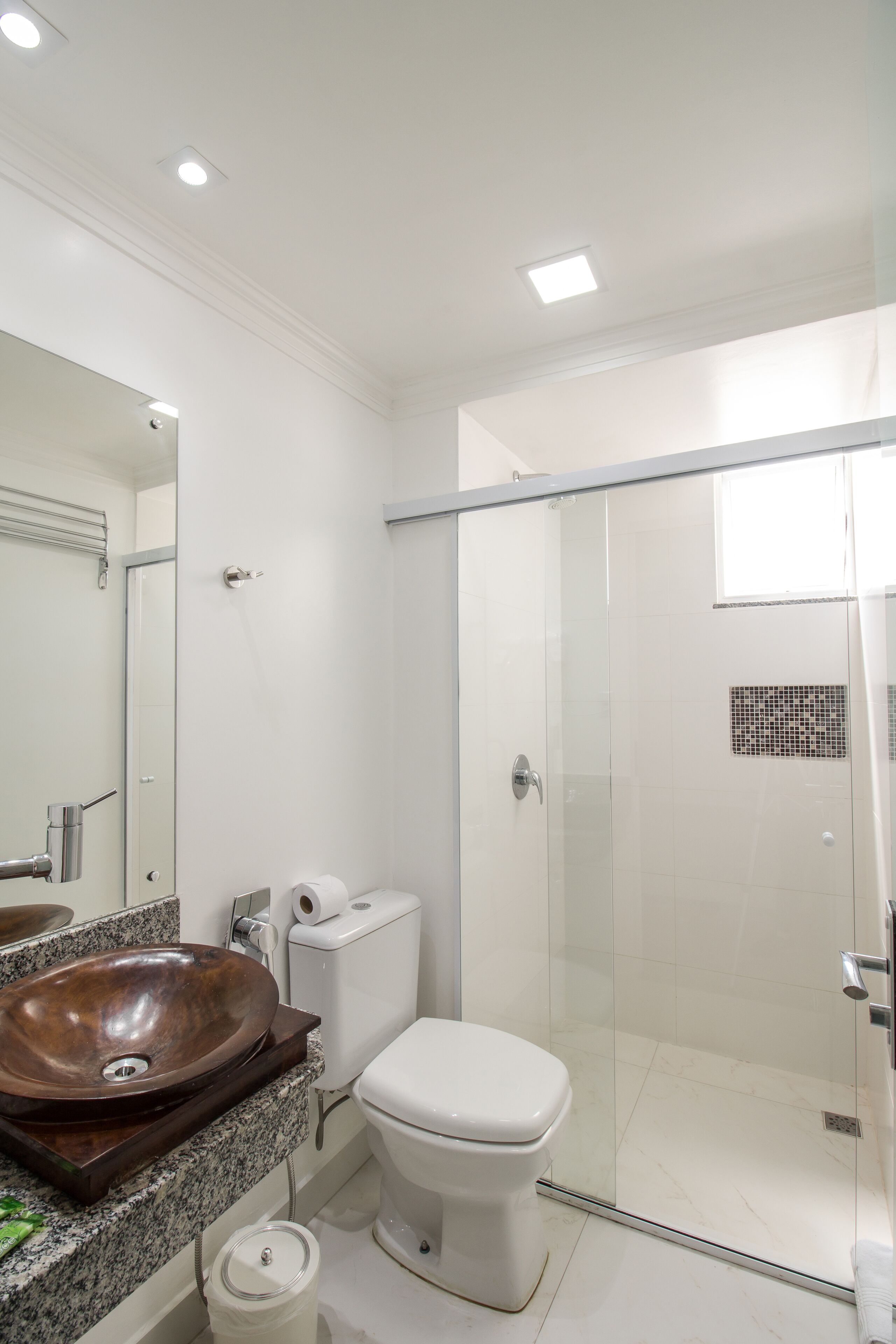 A modern bathroom with a glass-enclosed shower, a wooden vanity, and a white toilet.
