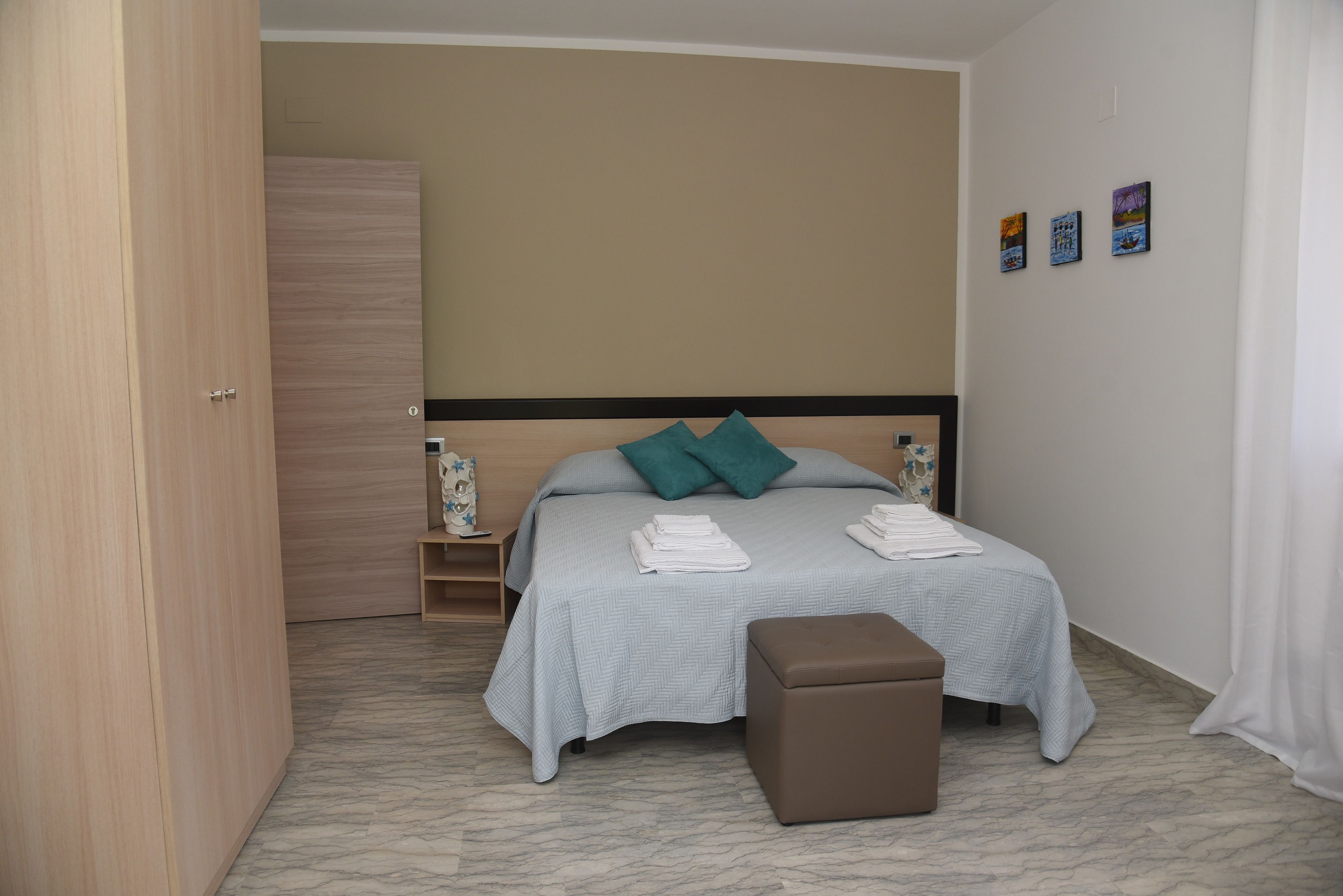 Un dormitorio con cama, mesita de noche, armario y pequeño banco.