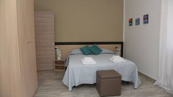 Un dormitorio con cama, mesita de noche, armario y pequeño banco.