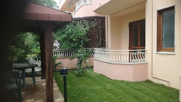 Um edifício residencial com um gramado bem cuidado, uma pérgula de madeira e uma varanda com guarda-corpo branco.