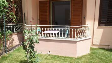 A small outdoor balcony with a metal railing, a table, and a chair.