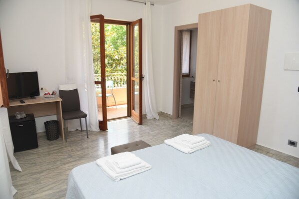 Une chambre d’hôtel comprenant un lit, un bureau, une chaise, une armoire et un balcon avec vue sur les arbres.