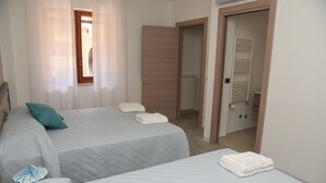 Een hotelkamer met twee bedden, een badkamer met een handdoekhouder en een deur naar een andere kamer.