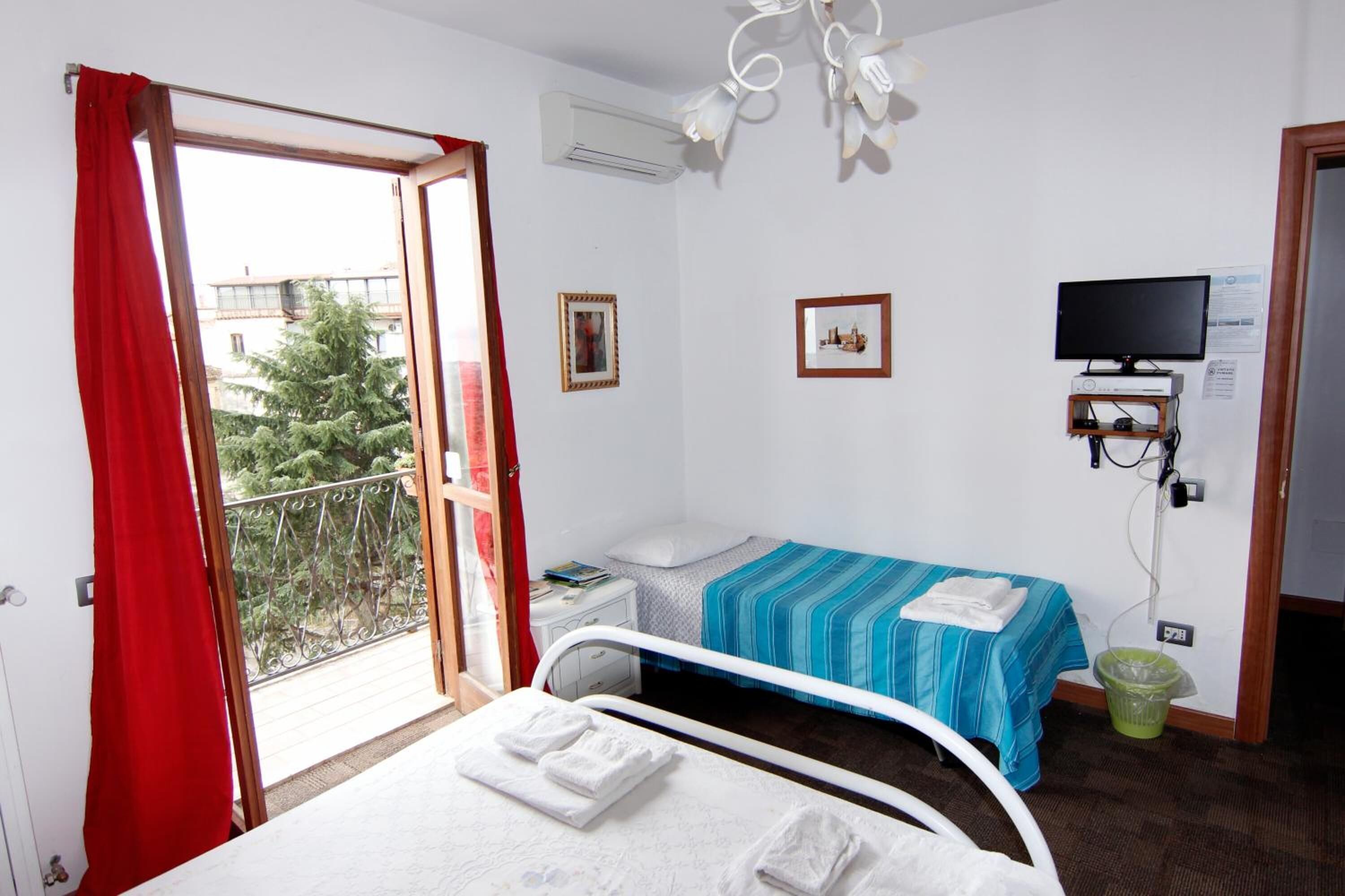 A hotel room with two beds, a TV, and a balcony with a view of trees.