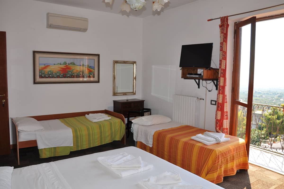 A hotel room with two beds, a TV, a painting, and a balcony with a view.