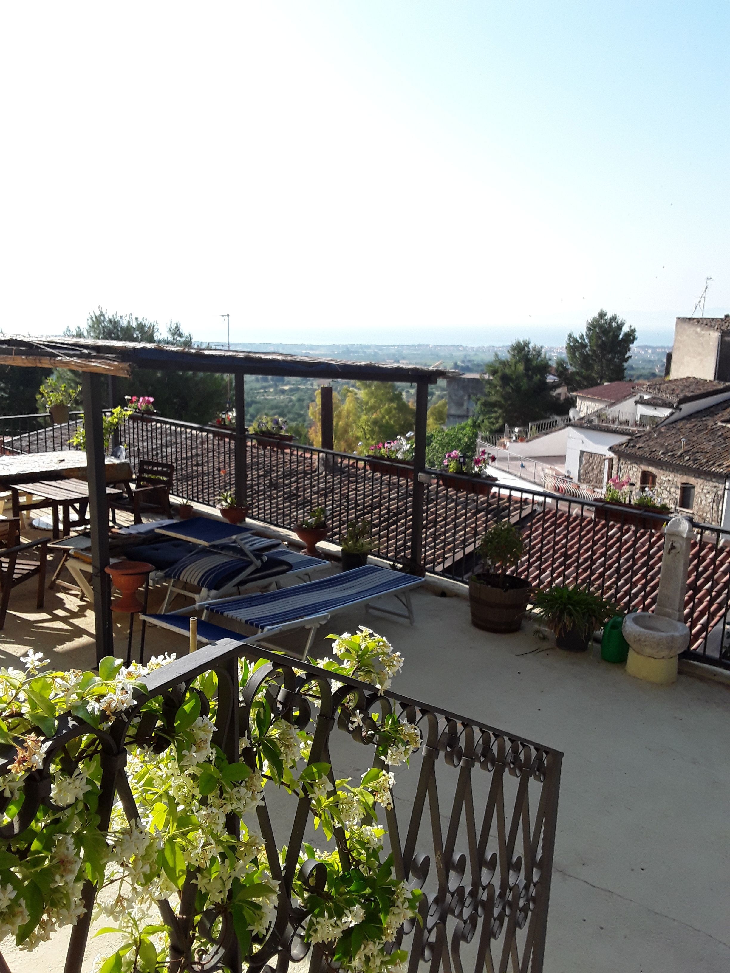 Eine Dachterrasse mit einer Pergola, Liegestühlen, Topfpflanzen und Blick auf die Stadtlandschaft.