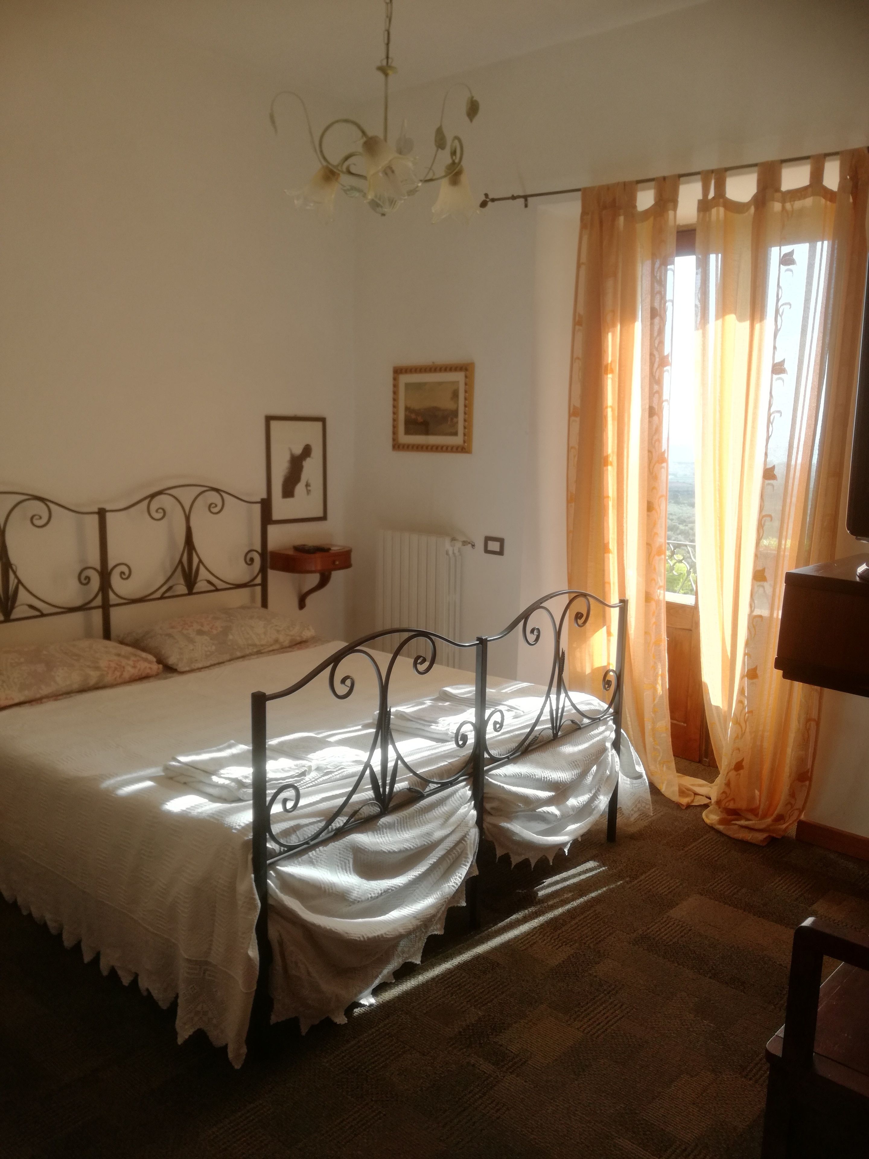Une chambre à coucher avec un lit, un radiateur, un tableau au mur et une fenêtre avec des rideaux.