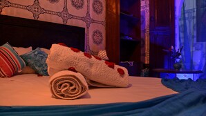 A neatly made bed with a rolled white towel and red rose, a striped pillow, and a blue pillow. - Riad Dar Leuleu (Marrakech)