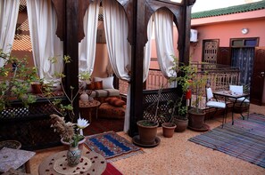 A cozy outdoor seating area with a sofa, chairs, and a table, surrounded by potted plants and a patterned rug. - Riad Dar Leuleu (Marrakech)