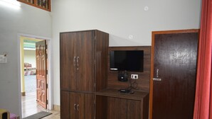 Una habitación con un armario de madera, un televisor sobre un mueble de madera y una puerta con cortina roja.