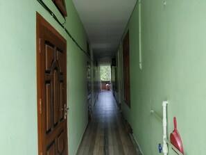 A corridor with wooden doors and a tiled floor, leading to a covered area with a view of greenery. - Bagori Resort (Golaghat)