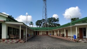 Un patio con suelo de baldosas, zonas de estar cubiertas y una alta torre de comunicaciones al fondo.