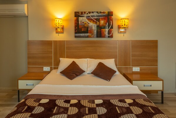 A neatly made bed with a patterned bedspread, two wall-mounted lamps, and a piece of abstract art above the bed.