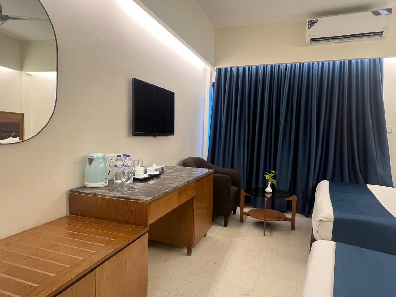 Quarto de hotel com secretária de madeira, cama, televisão e uma grande janela com cortinas.
